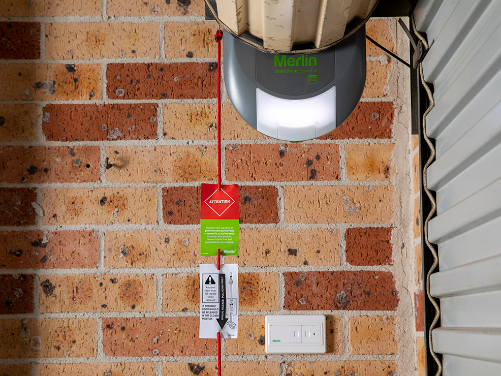 A merlin garage door opener is mounted on a brick wall.