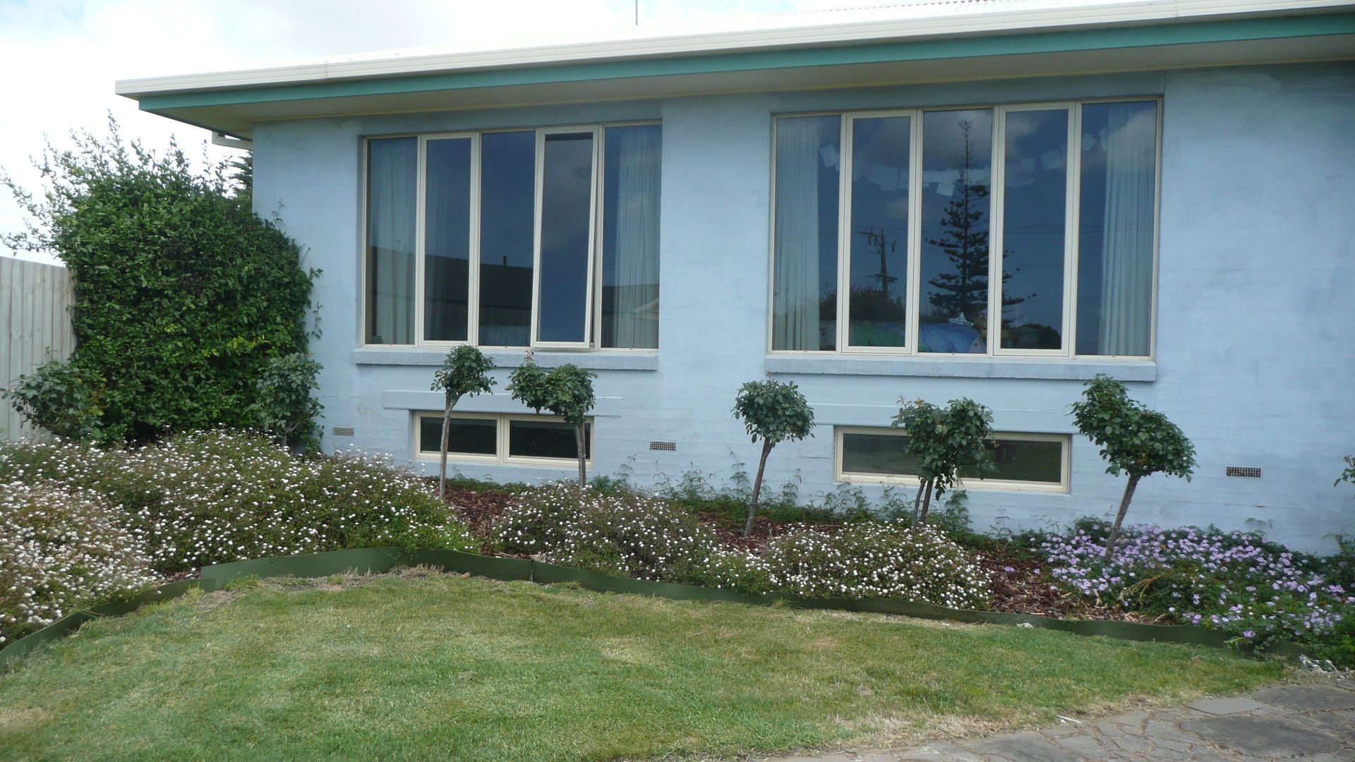 A blue house with a lot of windows and flowers in front of it