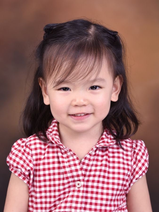 年輕的亞洲女孩，有著深色的頭髮，面帶微笑，穿著紅白格子襯衫。