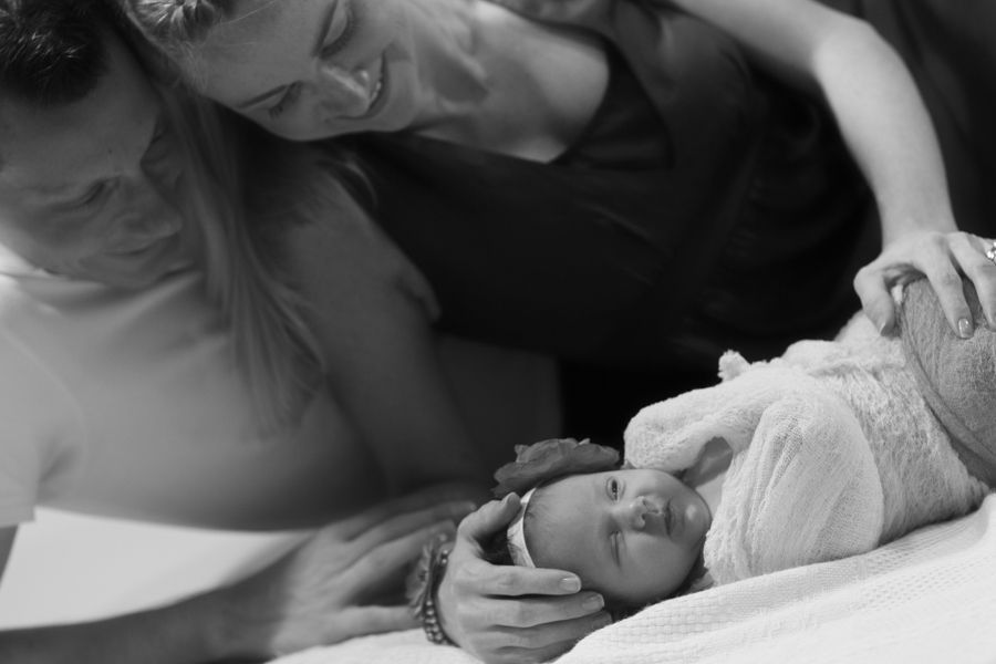 父母深情地看著躺在白色表面上的新生嬰兒，黑白照片。