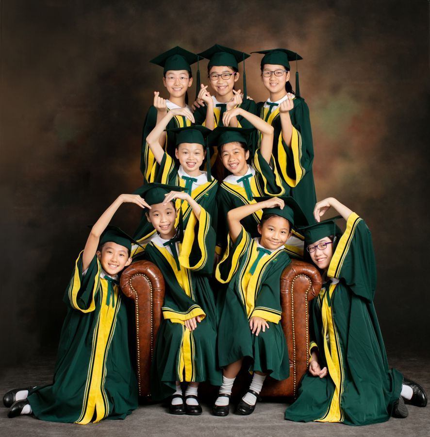 孩子們穿著綠色和黃色的畢業禮服，在棕色扶手椅上和周圍擺姿勢。