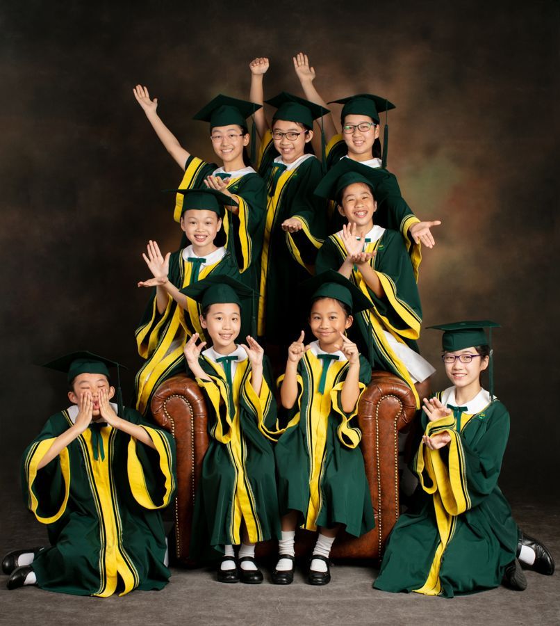 一群穿著綠色和黃色畢業禮服的孩子在工作室裡擺著嬉戲的姿勢。