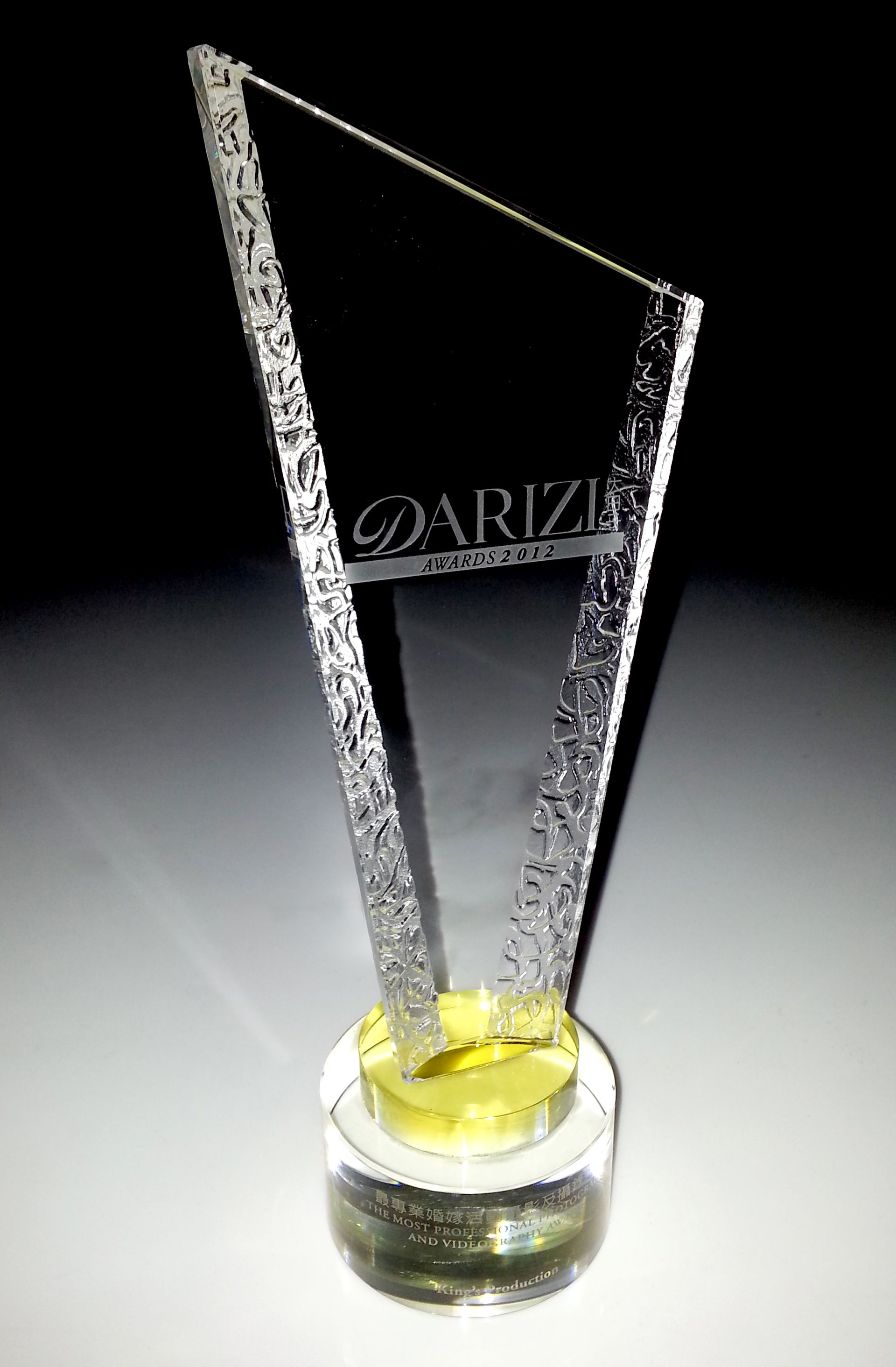 玻璃獎杯頂部為透明的傾斜設計,帶有“ARIZI”標誌,安裝在圓形、黃色中心底座上。