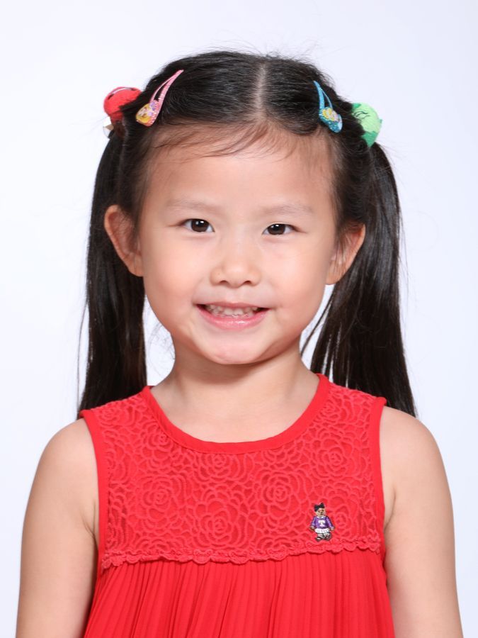 扎黑髮、身穿紅色洋裝的女孩，對著鏡頭微笑。