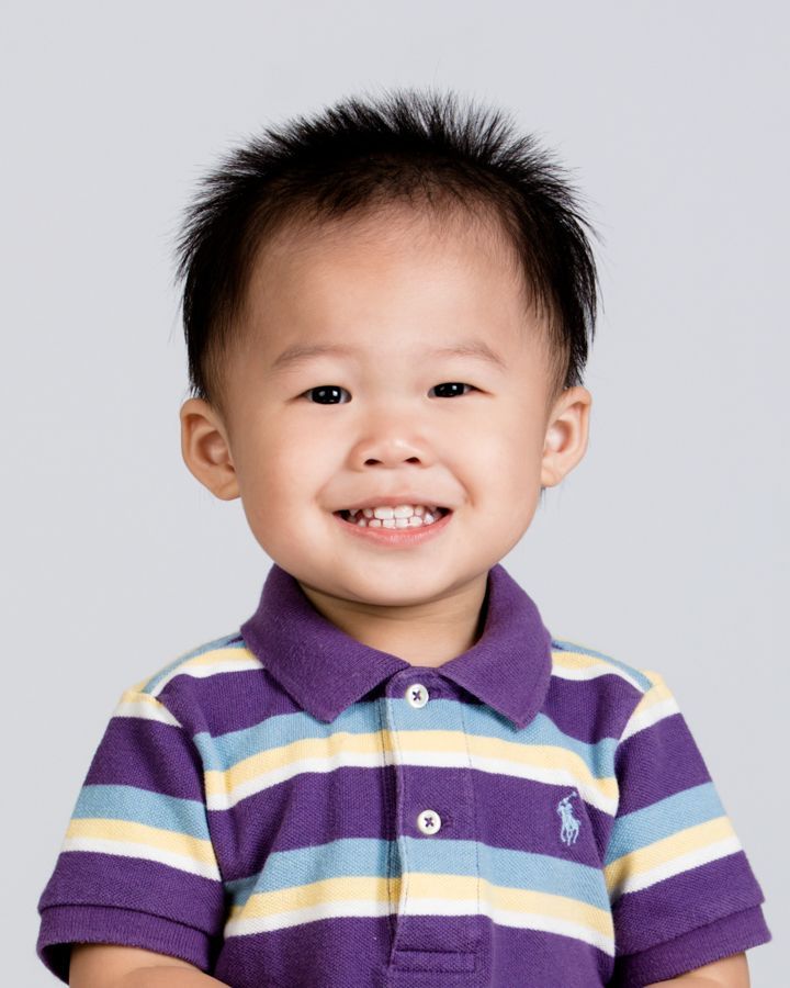 灰色背景下，黑髮、身穿紫色條紋 Polo 衫的幼兒面帶微笑。