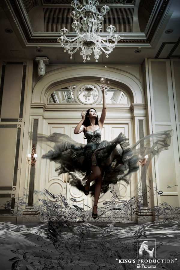 身著華麗長袍的女子在大廳中跳躍，伸手抓吊燈下漂浮的泡泡。