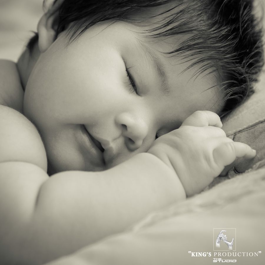 黑白相間、熟睡的嬰兒，臉頰靠在柔軟的表面上，手蜷縮在臉附近。