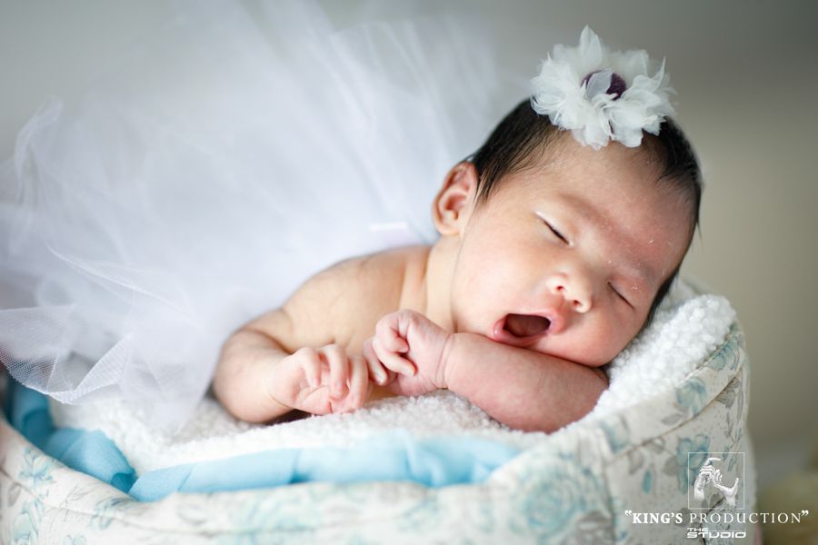 新生嬰兒睡在一個小軟墊籃子裡，穿著白色芭蕾舞短裙，戴著花冠。