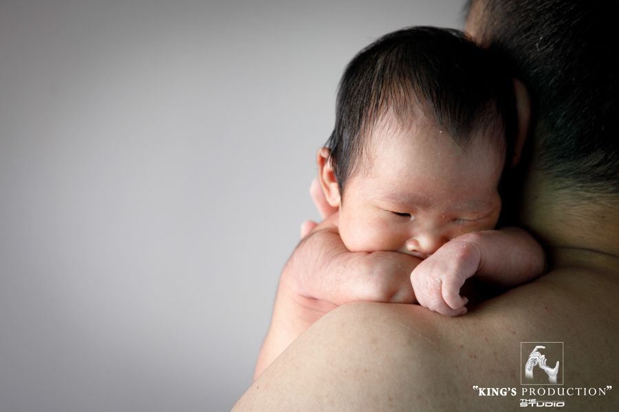 新生嬰兒睡在人的肩膀上，臉貼在皮膚上，膚色較淺。