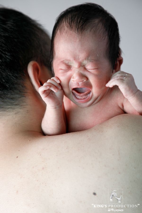 室內，新生兒被抱在人的肩膀上哭泣。