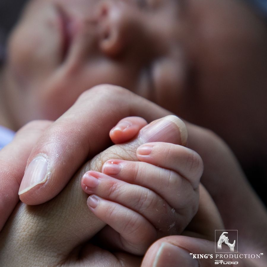 嬰兒的小手緊握著大人的手指；背景模糊，有一張臉，色調溫暖。