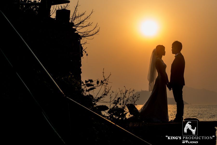 日落時分，一對新婚夫婦在水邊手牽手的剪影。