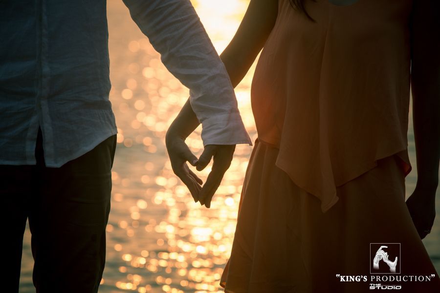 一對情侶手牽手，手指組成一顆心。夕陽西下，水面上。