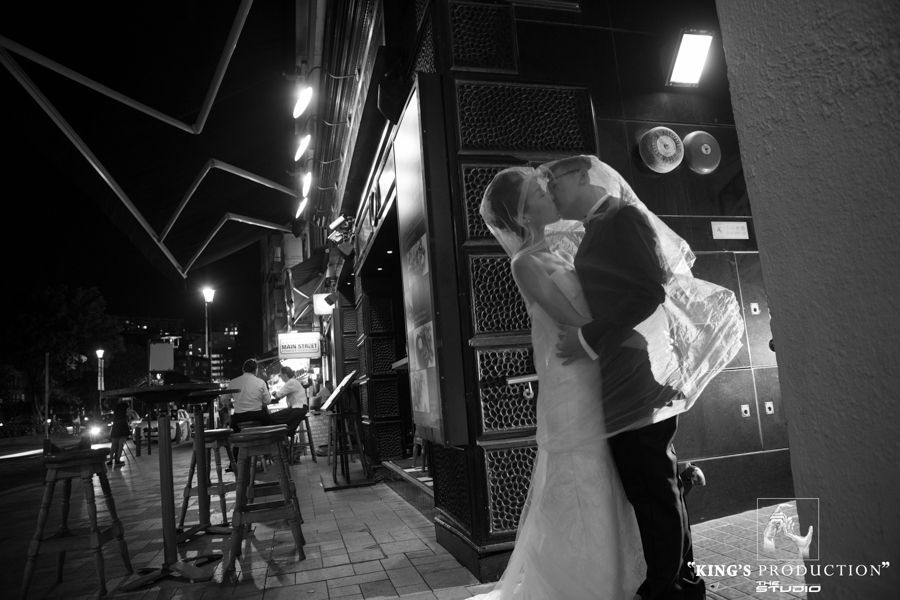 夜晚，新娘和新郎在燈光明亮的酒吧外熱情地接吻。
