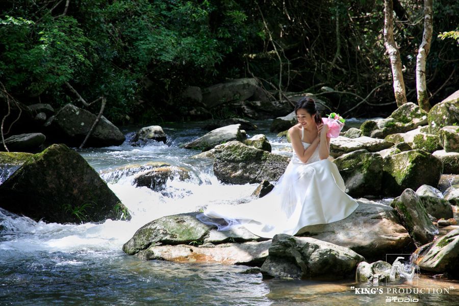 身著婚紗的女子坐在河邊的岩石上。背景是鬱鬱蔥蔥的綠色森林。