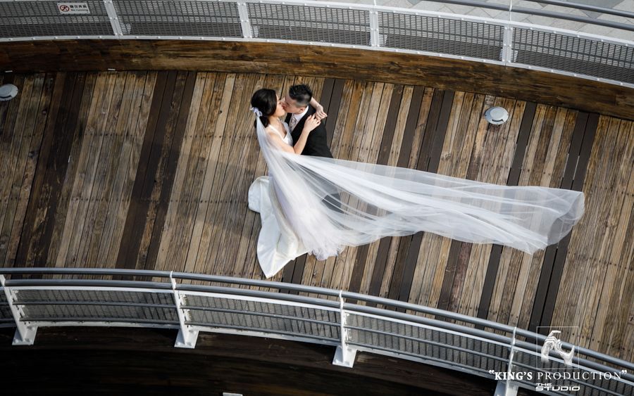 新娘和新郎在木碼頭上接吻，面紗飄揚；陽光投下陰影。