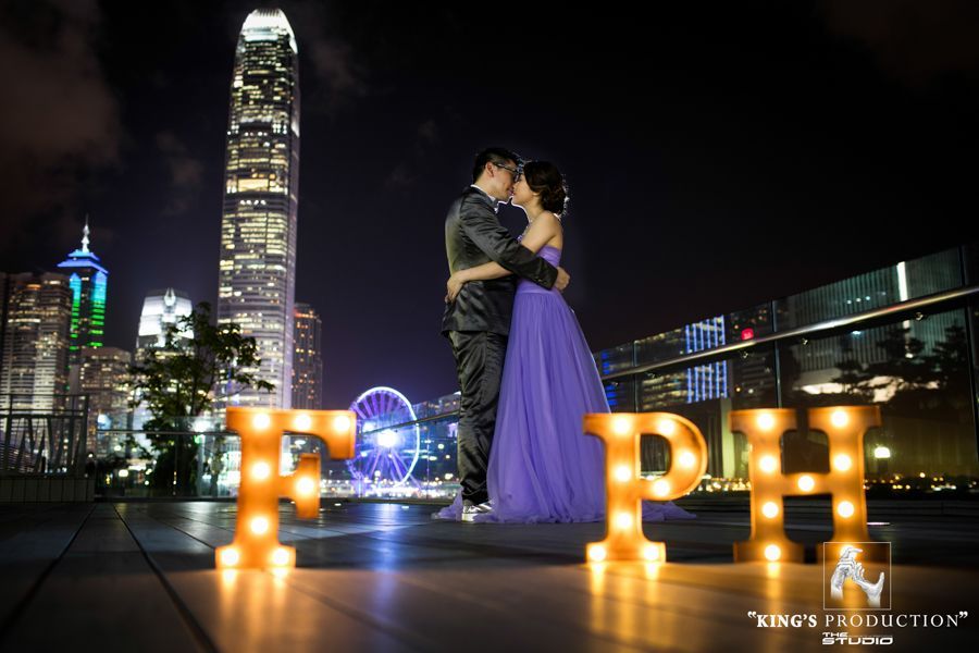 夜晚，一對情侶在城市天際線前擁抱，身旁是發光的「FPH」字母。