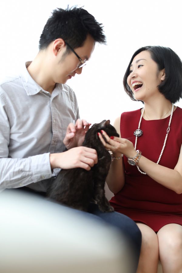 一對情侶撫摸著一隻黑貓。女子笑著，男子則輕撫貓背。室內。