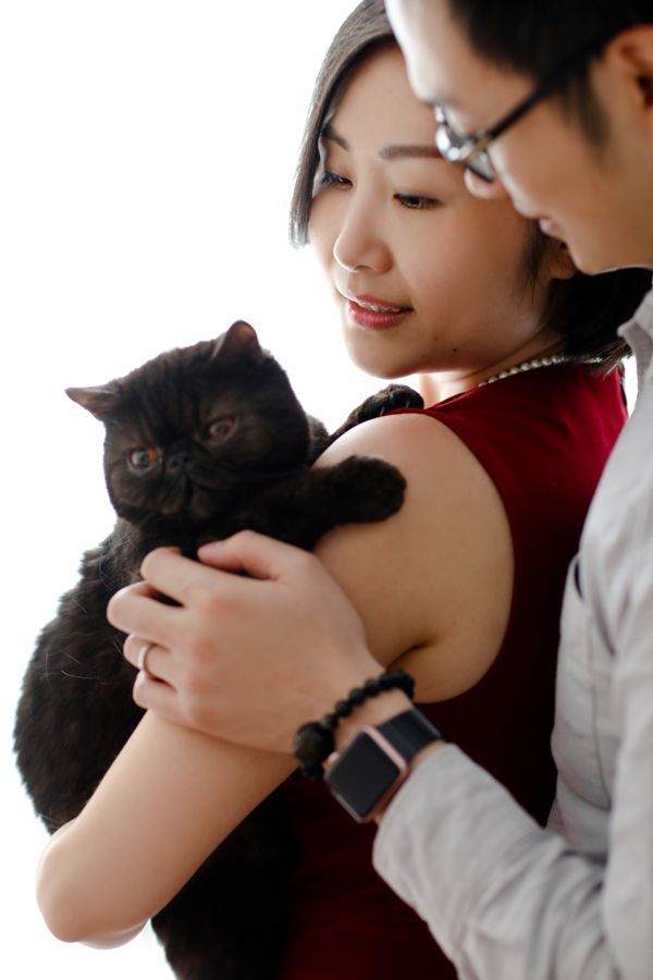 穿紅衣服的女人抱著黑貓，戴眼鏡的男人在一旁看著。