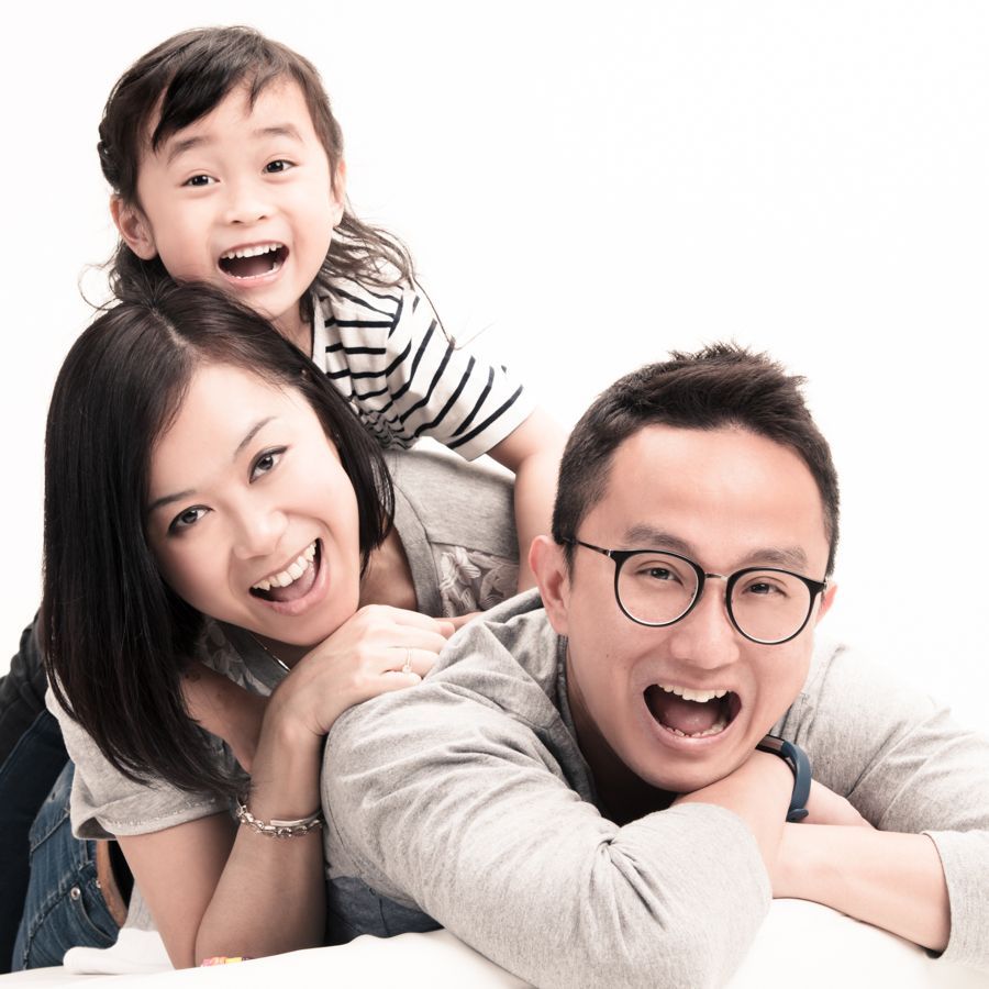 一家三口笑容滿面，擺出開心的姿勢。孩子坐在父母背上；白色背景。