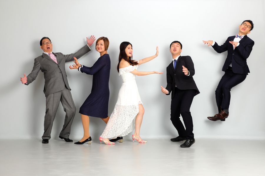 六個人穿著正式服裝，在淺灰色牆壁前擺出有趣、動感的姿勢。