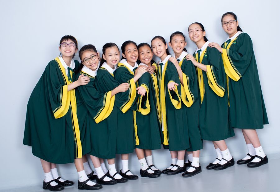 九名身穿綠色畢業禮服的亞洲女孩微笑著在白色牆壁前擺姿勢。