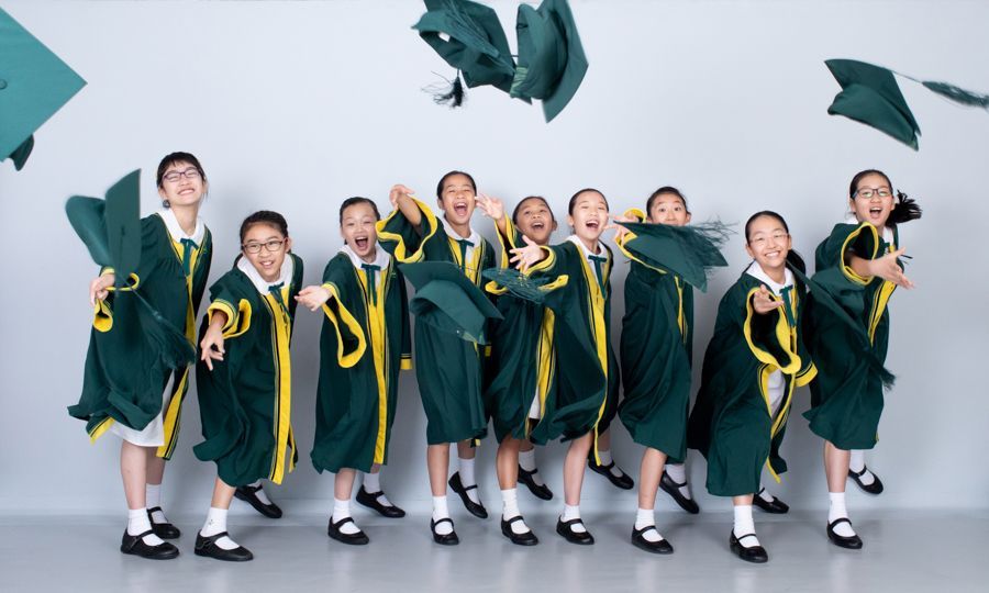 一群身穿綠色畢業禮服的微笑女孩將帽子拋向空中。