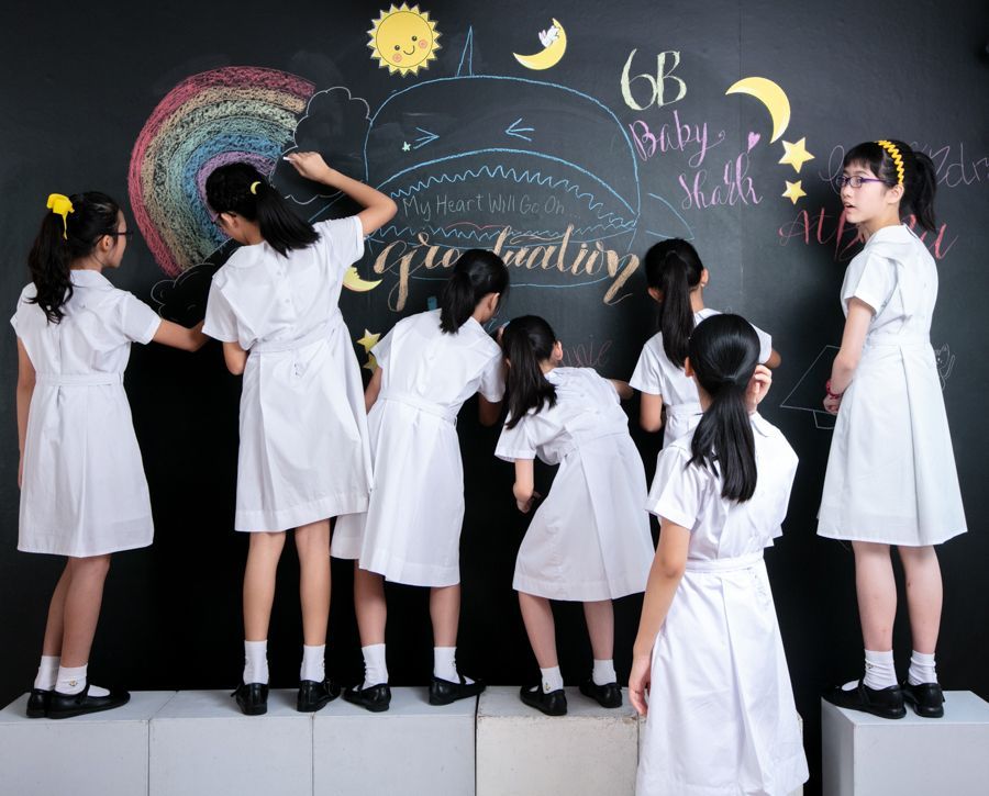 身穿白色校服的女孩們在黑板上畫著畢業藝術畫。