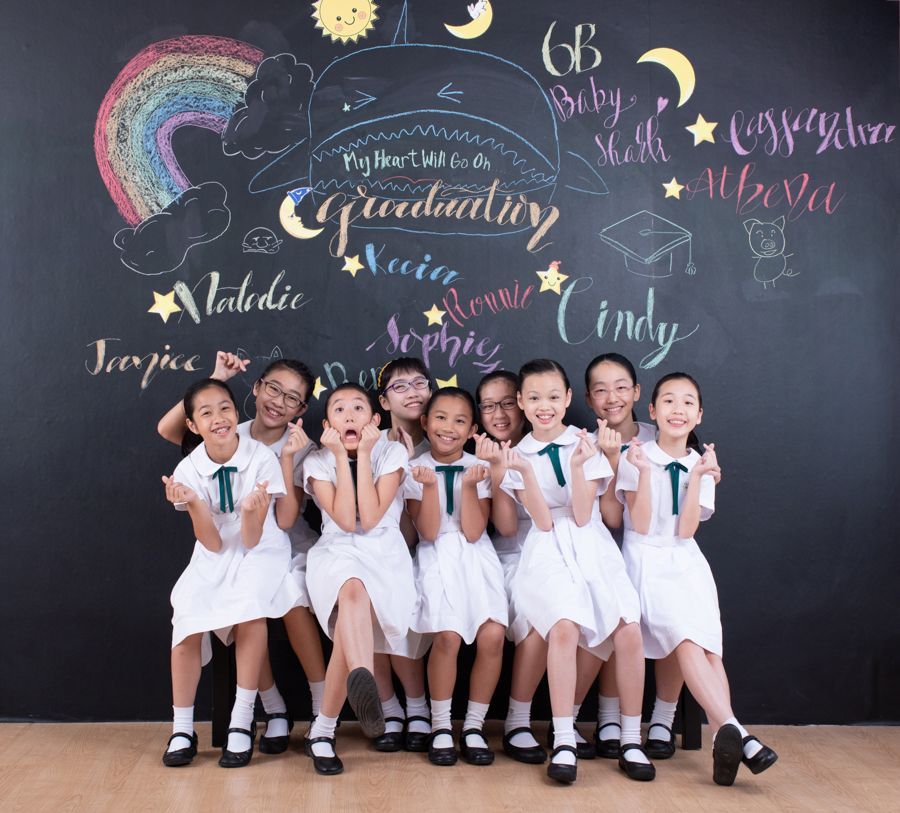 一群身穿白色制服的微笑女孩在彩虹畢業黑板前擺姿勢。