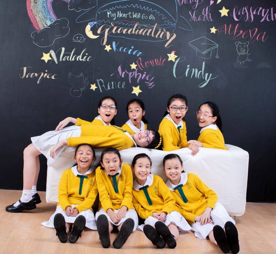 一群身穿黃色制服的微笑女孩在畢業主題的黑板前擺姿勢。