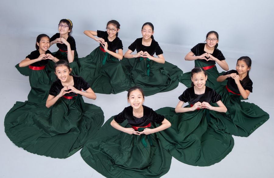 一群穿著綠色裙子和黑色上衣的年輕女孩，用手做出心形。