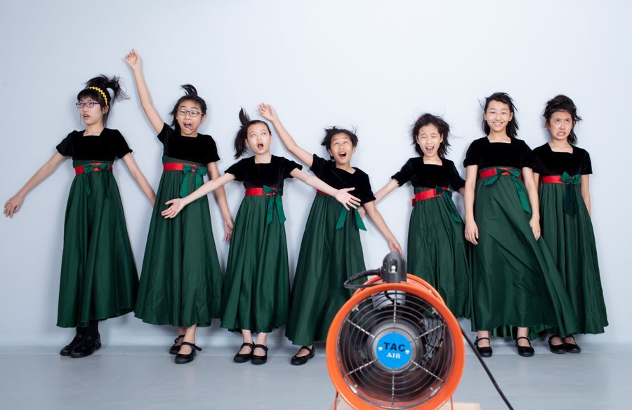 一群身穿綠色洋裝和黑色上衣的女孩在粉絲麵前擺出誇張的姿勢。