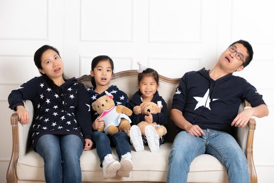 一家四口坐在奶油色的沙發上，都穿著星星圖案的連帽衫，看起來很疲憊，擺姿勢拍照。