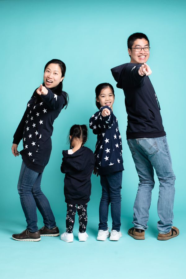 一家四口身穿星星毛衣，在藍綠色背景下指著指點點，面帶微笑。