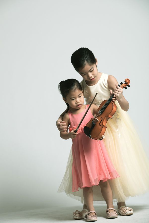 兩個穿著禮服的小女孩正在學習拉小提琴。其中一個正在教另一個。