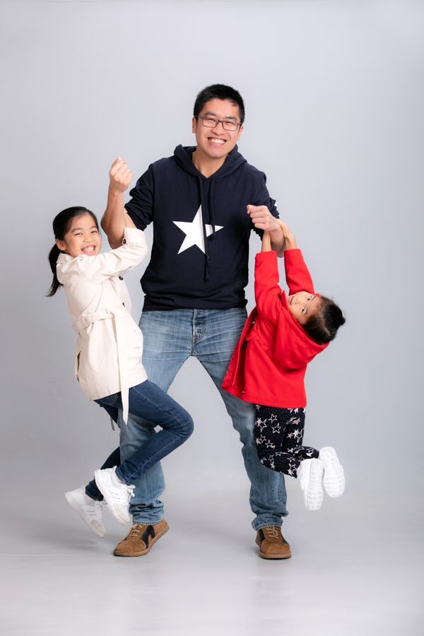 父親抱著兩個女兒，她們個個笑容滿面，幸福快樂。工作室拍攝，灰色背景。