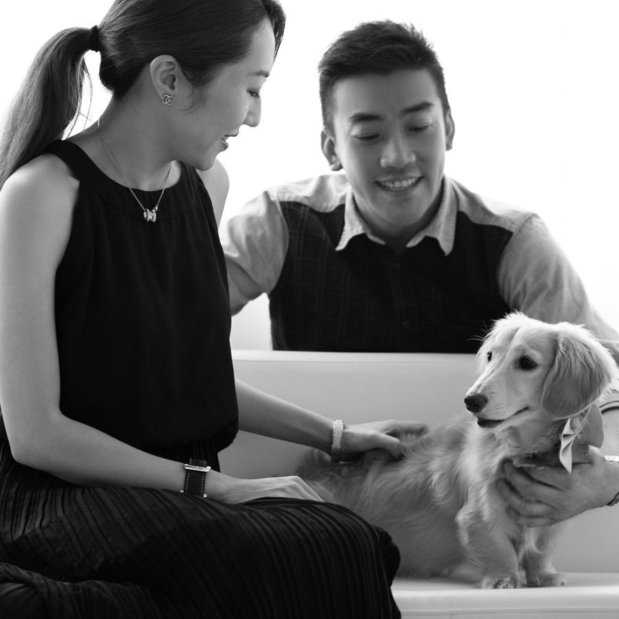 一名女子正在撫摸一隻狗，而一名男子則坐在白色沙發上微笑地看著。