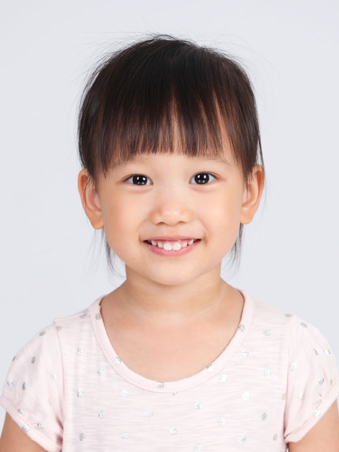 白色背景下，一位留著瀏海、穿著淺粉紅色襯衫、面帶微笑的年輕亞洲女孩。