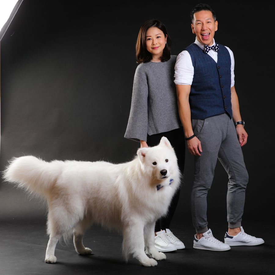 一名女子、一名男子和一隻大白狗在黑色背景前擺姿勢。男子身穿背心，繫著領結，狗狗也戴著領結。