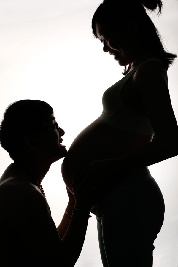 孕婦和伴侶的剪影。男人親吻她的肚子，而她則低頭微笑。