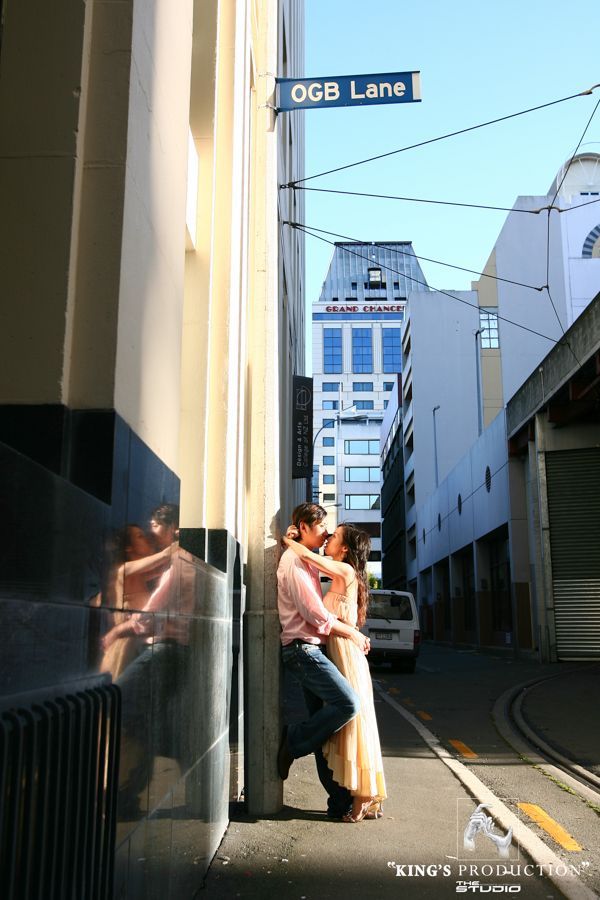 一對情侶在一條狹窄的城市小巷中擁抱，路牌上寫著「OGB Lane」。