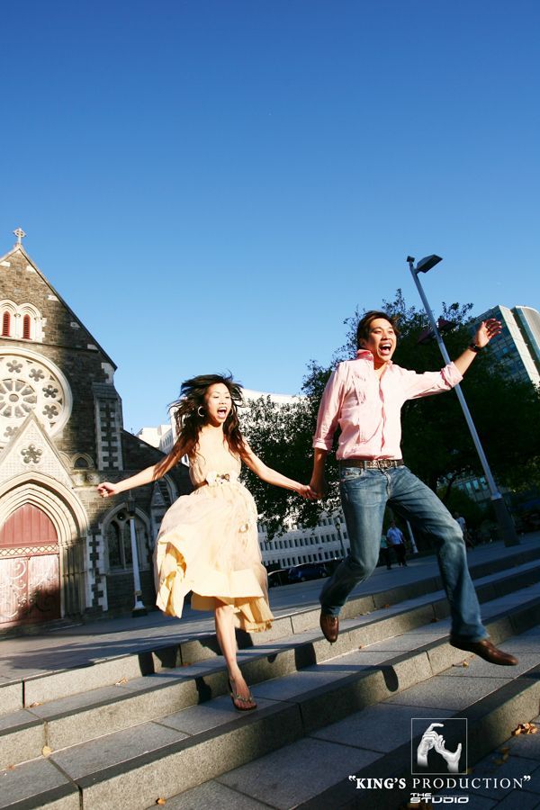 一對情侶手牽手，從教堂前的階梯跳下來。陽光明媚的日子。