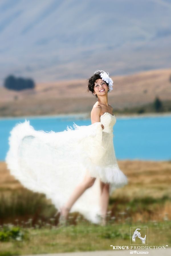 新娘穿著白色禮服，在碧綠的湖泊旁旋轉，微笑，背景是山脈。