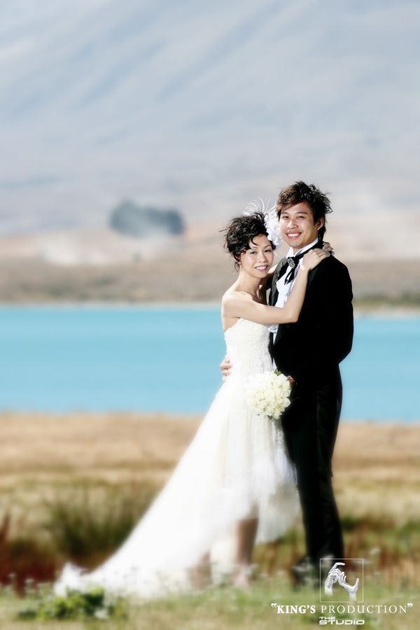 身著婚禮服裝的新娘和新郎在湖邊戶外擁抱，背景是山。