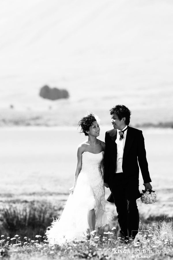 新郎新娘手牽手走在田野裡，互相凝視。黑白照片。