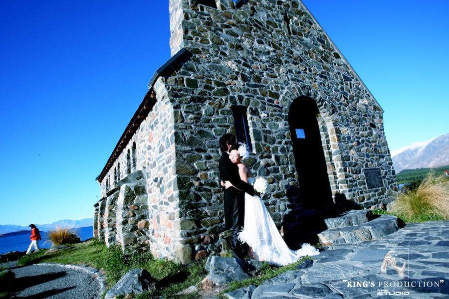 在陽光明媚的日子，新娘和新郎在一座石頭教堂前接吻。