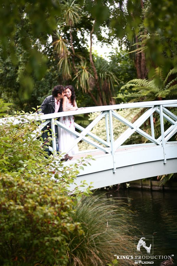 一對情侶在鬱鬱蔥蔥的公園裡，在淺藍色的水橋上接吻。