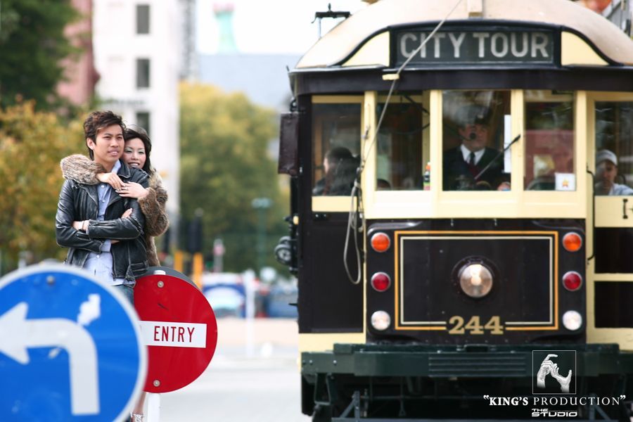 一對情侶在路牌附近擁抱，背景是城市觀光電車。