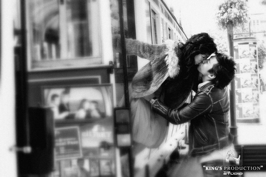 一對情侶在戶外、相框旁熱吻；黑白。