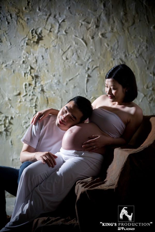 一位孕婦和一位男士坐在一起，男士聽著孕婦肚子裡的聲音。他們坐在工作室的沙發上。